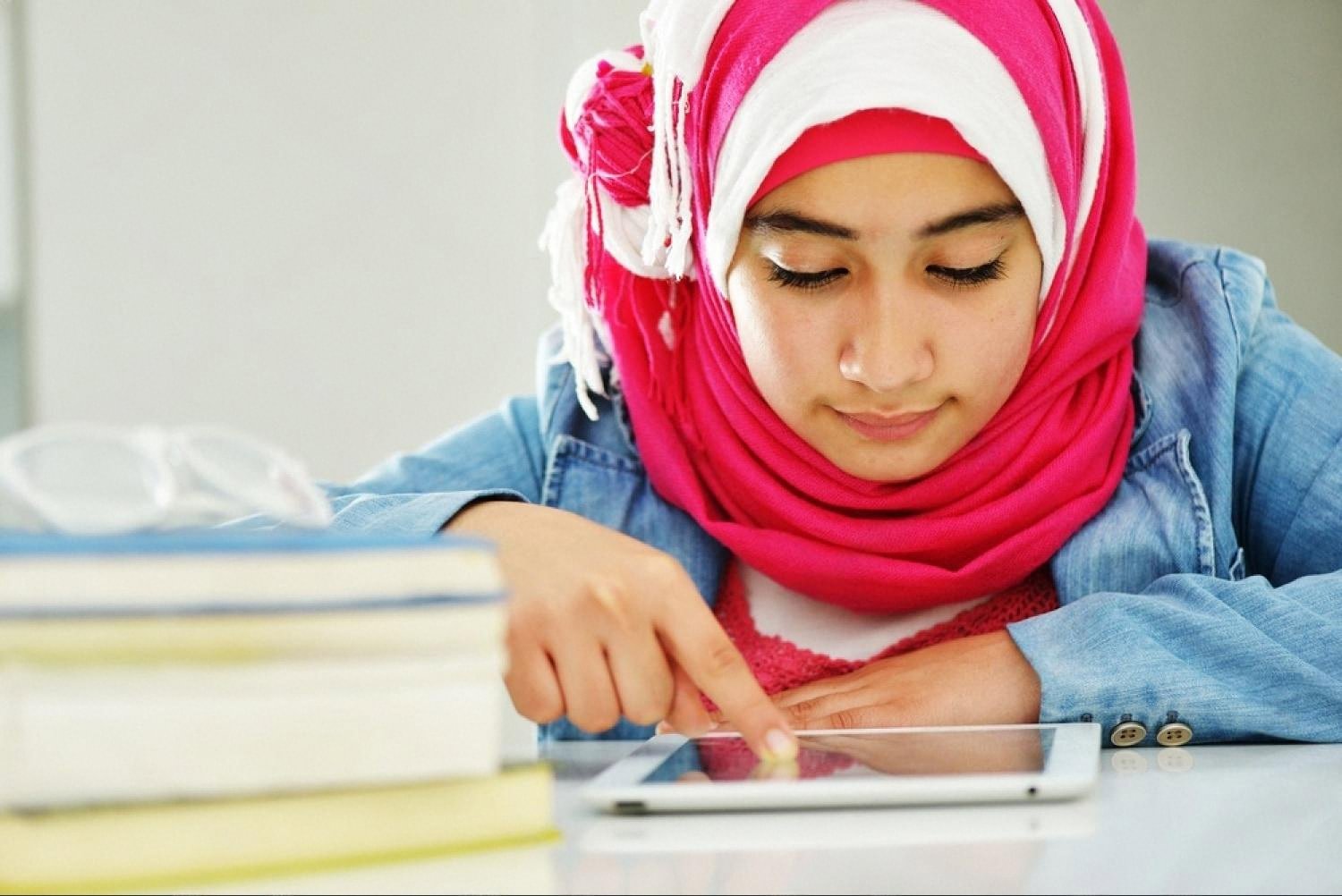 Young student in a hijab using a tablet with textbooks stacked beside her at an Indian school in Ajman